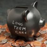long-term care in chalk on black piggy bank with change on table
