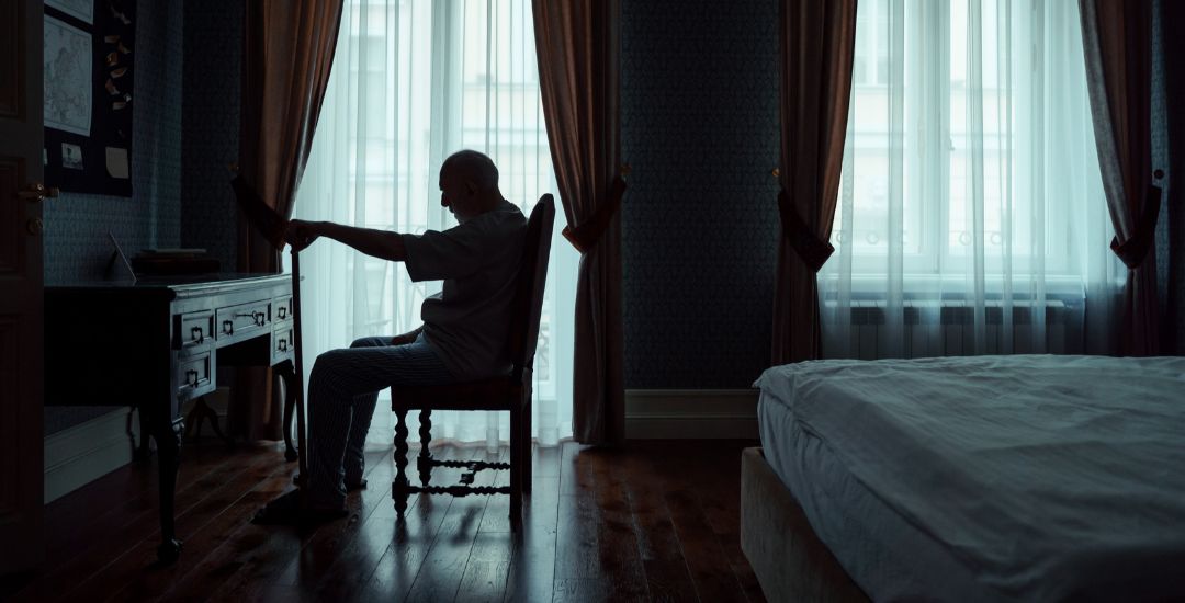 elderly man sitting alone in bedroom