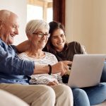 elderly couple with adult daughter looking at laptop